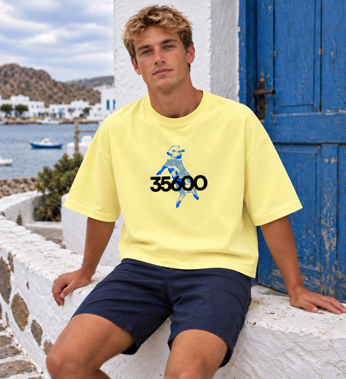 Modelo con la camiseta amarilla Baifo 35600 sentado junto a una puerta azul y el mar.