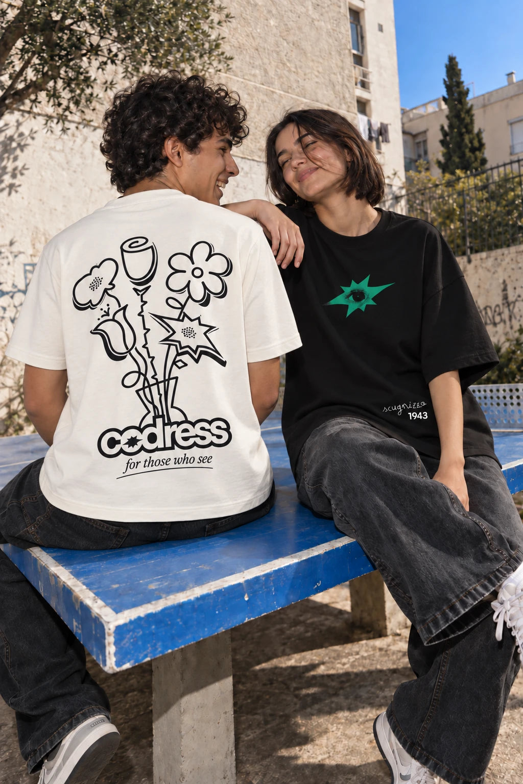 Dos amigos con las camisetas Flowers y Scugnizzo de CODRESS sobre una mesa de ping-pong azul.